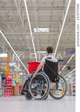 A Caucasian woman in a wheelchair shopping in a supermarket. A Caucasian woman in a wheelchair shopping in a supermarket. 142874366