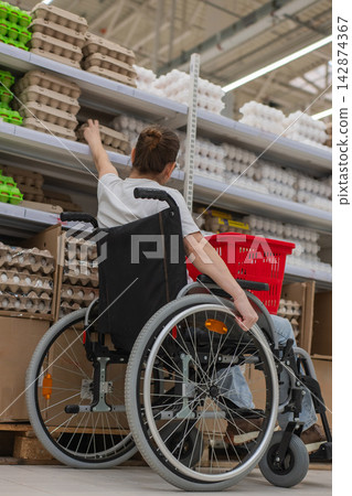 A Caucasian woman in a wheelchair shopping in a supermarket. A Caucasian woman in a wheelchair shopping in a supermarket. 142874367