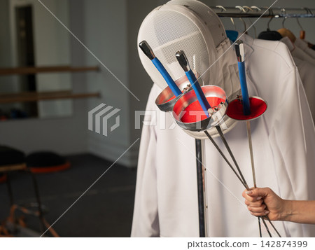 Fencing uniforms and masks hang on hangers. No people. Fencing uniforms and masks hang on hangers. No people. 142874399