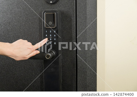 A woman opens a modern smart door lock with a digital keypad using a code. A woman opens a modern smart door lock with a digital keypad using a code. 142874400