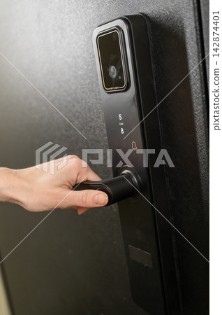 A woman opens a modern smart door lock with a digital keypad and biometric fingerprint access. A woman opens a modern smart door lock with a digital keypad and biometric fingerprint access. 142874401