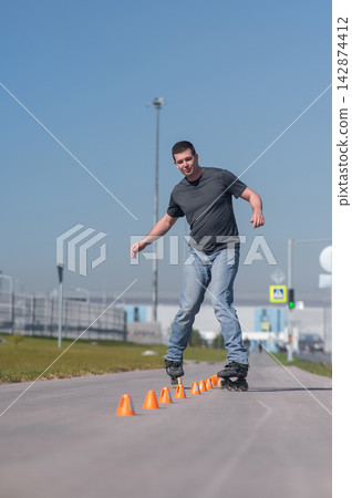 A Caucasian man rollerblades around the slalom course. A Caucasian man rollerblades around the slalom course. 142874412