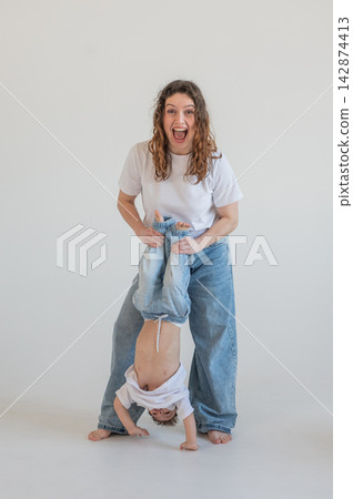 A Caucasian woman holds her two-year-old son by the legs. The boy and mother are playing around. A Caucasian woman holds her two-year-old son by the legs. The boy and mother are playing around. 142874413