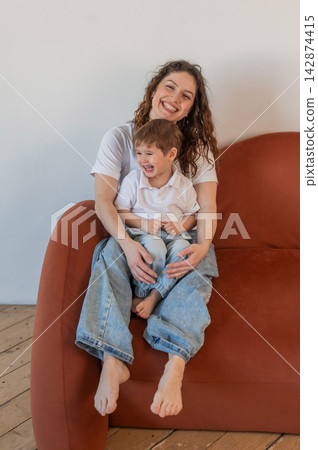 A Caucasian woman and her two-year-old son hug while sitting on a sofa. A Caucasian woman and her two-year-old son hug while sitting on a sofa. 142874415