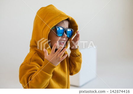 Portrait of a two-year-old boy wearing sunglasses and an orange hoodie. Portrait of a two-year-old boy wearing sunglasses and an orange hoodie. 142874416