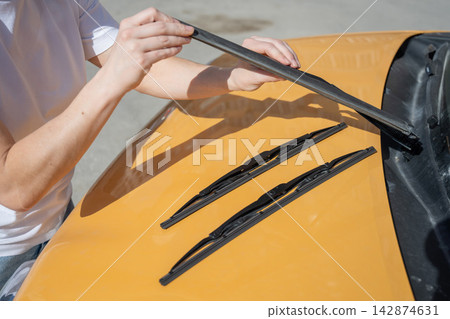 A woman replaces old windshield wipers with new ones on a car. 142874631