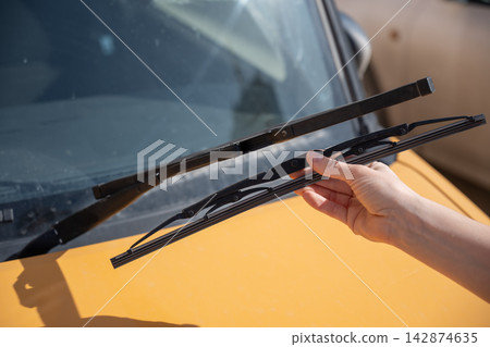 A woman replaces old windshield wipers with new ones on a car. A woman replaces old windshield wipers with new ones on a car. 142874635