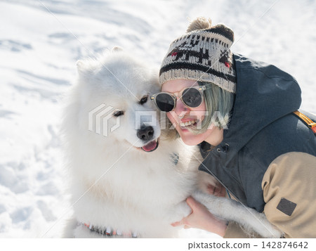 Portrait of a Smiling woman holding fluffy samoyed dog in snowy winter park. Portrait of a Smiling woman holding fluffy samoyed dog in snowy winter park. 142874642