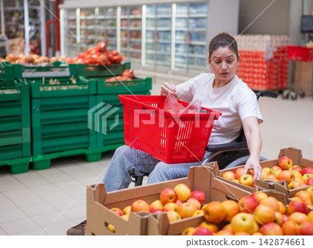 A Caucasian woman in a wheelchair buys apples at a supermarket. A Caucasian woman in a wheelchair buys apples at a supermarket. 142874661