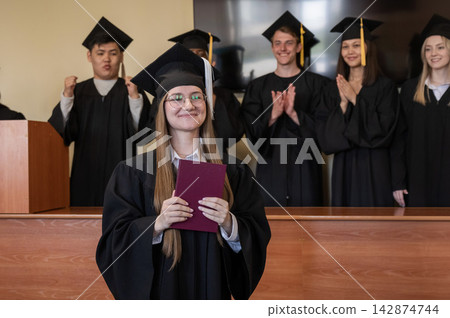Happy Caucasian woman holds red diploma and classmates support her. Happy Caucasian woman holds red diploma and classmates support her. 142874744