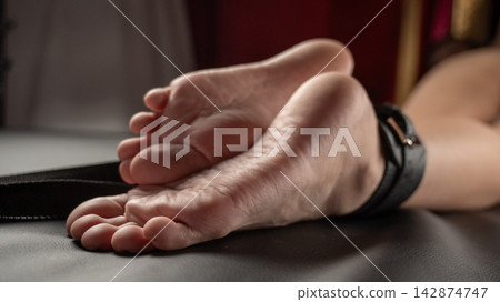 Women's legs in leather shackles. BDSM fetish. Women's legs in leather shackles. BDSM fetish. 142874747