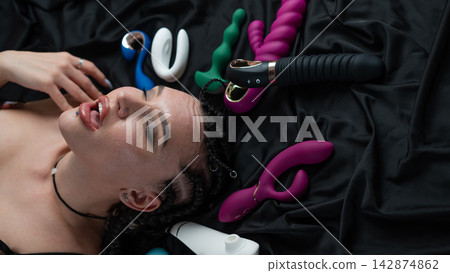 Portrait of Caucasian woman lying on bed among sex toys. Portrait of Caucasian woman lying on bed among sex toys. 142874862