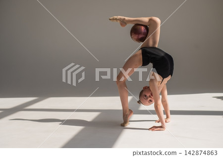 Little gymnast posing with a ball on a white background.  142874863