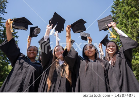 Young women of different nationalities pull graduation caps up. Young women of different nationalities pull graduation caps up. 142874875