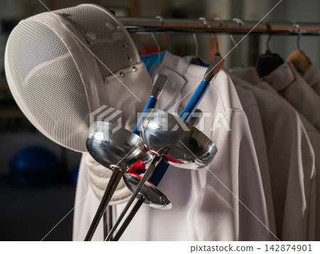 Fencing uniforms and masks hang on hangers. No people.  142874901