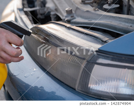Close-up of a man washing car headlights with spray cleaner. Close-up of a man washing car headlights with spray cleaner. 142874904