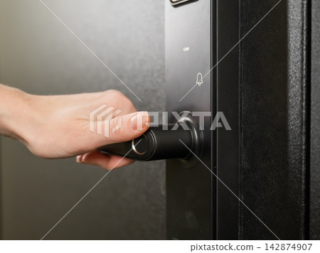 A woman opens a modern smart door lock with a digital keypad and biometric fingerprint access. A woman opens a modern smart door lock with a digital keypad and biometric fingerprint access. 142874907
