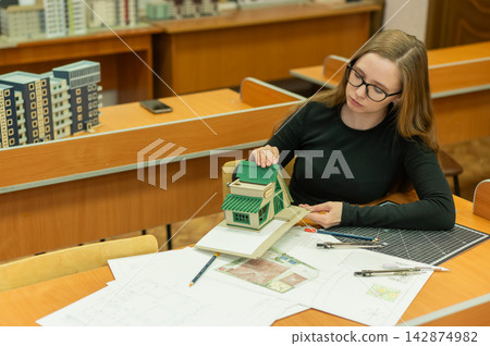 Caucasian young woman making a model of a building. Student of the construction university. Caucasian young woman making a model of a building. Student of the construction university. 142874982