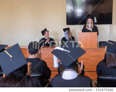 A young woman stands at the lectern and delivers a graduation speech to her classmates. A young woman stands at the lectern and delivers a graduation speech to her classmates. 142875080