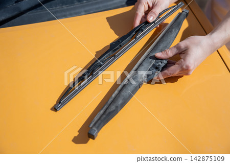 A woman replaces old windshield wipers with new ones on a car. A woman replaces old windshield wipers with new ones on a car. 142875109
