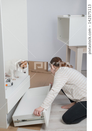A Caucasian woman assembles furniture with her cute dog. A Caucasian woman assembles furniture with her cute dog. 142875113