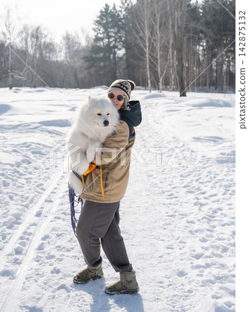 Smiling woman holding fluffy samoyed dog in snowy winter park. Smiling woman holding fluffy samoyed dog in snowy winter park. 142875132