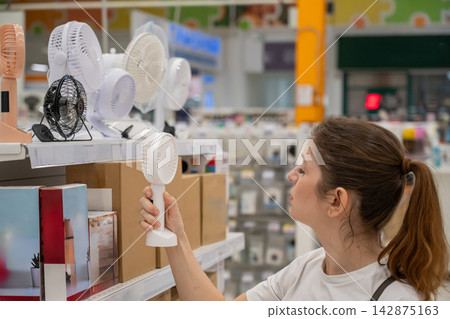 A Caucasian woman chooses a fan in a supermarket. A Caucasian woman chooses a fan in a supermarket. 142875163