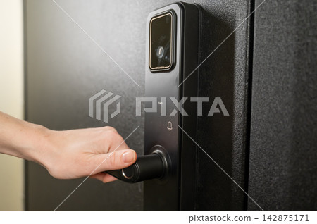 A woman opens a modern smart door lock with a digital keypad and biometric fingerprint access. A woman opens a modern smart door lock with a digital keypad and biometric fingerprint access. 142875171