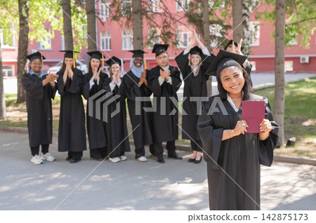 Young African woman holds diploma while classmates applaud her.  142875173