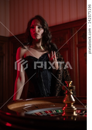 A beautiful brunette in a black dress at the casino roulette wheel. A beautiful brunette in a black dress at the casino roulette wheel. 142875196