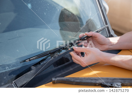 A woman replaces old windshield wipers with new ones on a car. 142875270
