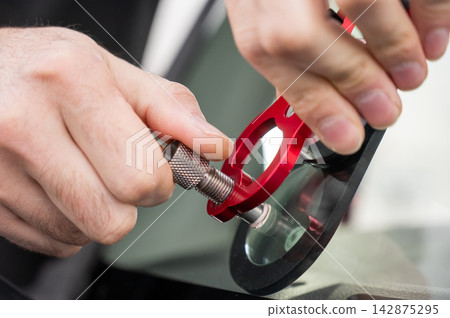 A technician injects resin into a windshield crack.  142875295
