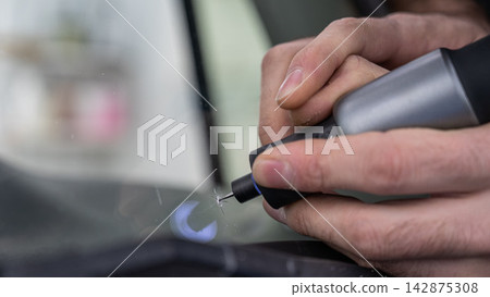 A technician drills a hole during a car windshield chip repair. 142875308