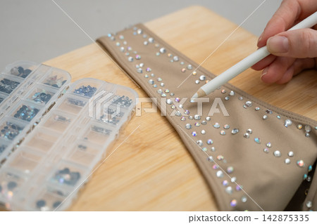 A woman decorates her gymnastics costume with rhinestones. Rhythmic gymnastics. A woman decorates her gymnastics costume with rhinestones. Rhythmic gymnastics. 142875335
