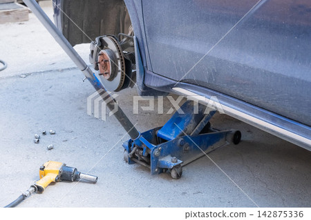 A car without a wheel on a jack. A car without a wheel on a jack. 142875336