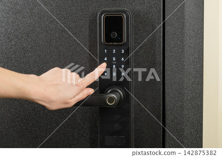 A woman opens a modern smart door lock with a digital keypad using a code. A woman opens a modern smart door lock with a digital keypad using a code. 142875382