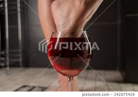 Foot fetish. A woman dips her toes in a glass of red wine. Foot fetish. A woman dips her toes in a glass of red wine. 142875420