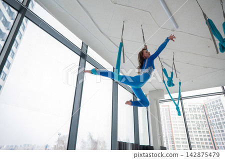 A Caucasian woman performs acrobatic exercises on a hammock. Aerial yoga. A Caucasian woman performs acrobatic exercises on a hammock. Aerial yoga. 142875479