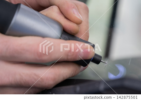 A technician drills a hole during a car windshield chip repair. 142875501