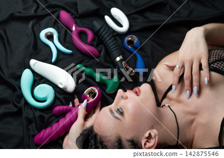 Portrait of Caucasian woman lying on bed among sex toys. Portrait of Caucasian woman lying on bed among sex toys. 142875546