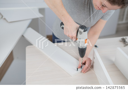 A Caucasian woman uses a screwdriver to tighten a screw while assembling a cabinet. A Caucasian woman uses a screwdriver to tighten a screw while assembling a cabinet. 142875565