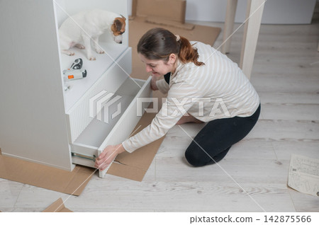 A Caucasian woman assembles furniture with her cute dog. 142875566