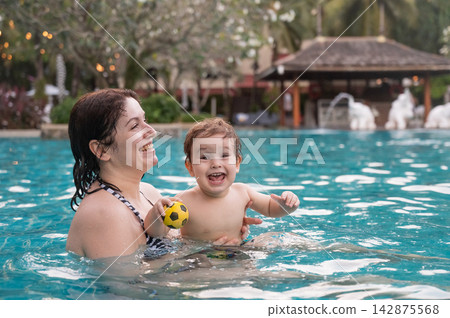 Caucasian woman holds son while swimming in pool on vacation. Caucasian woman holds son while swimming in pool on vacation. 142875568