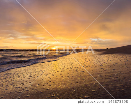 Sunset over the ocean at a sandy beach with gentle waves 142875598