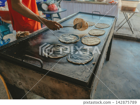 Vendor preparing tortillas on a grill. Vendor's hands grilling corn tortillas Vendor preparing tortillas on a grill. Vendor's hands grilling corn tortillas 142875789