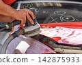 Grinder in the hands of a man who sharpen a car varnish in the car shop. 142875933
