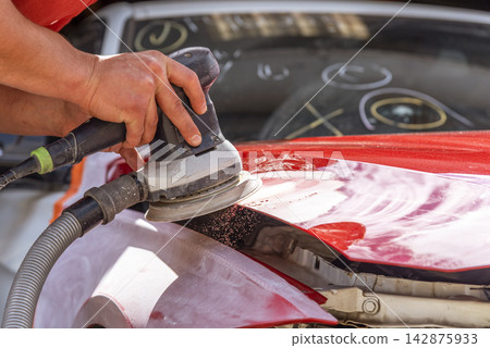 Grinder in the hands of a man who sharpen a car varnish in the car shop. Grinder in the hands of a man who sharpen a car varnish in the car shop. 142875933