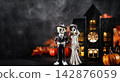 Skeleton bride and groom figurines beside glowing haunted house, pumpkins and smoke. Gothic Halloween wedding decorations on dark background with ample copy space. Halloween holiday card. 142876059