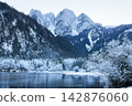Scenic winter view of Gosau lake and Gosaukamm mountain range in Austria with snow covered trees and cold lake. Alpine mountain snow covered and calm winter lake surrounded by frosted pine forest. 142876060
