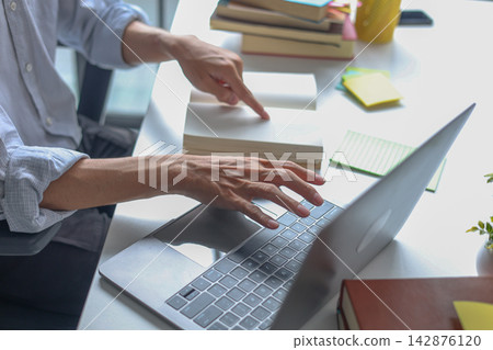 A young male tutor teacher explains a lesson during a virtual class with laptop and books on the table. A young male tutor teacher explains a lesson during a virtual class with laptop and books on the table. 142876120